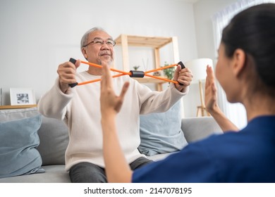 Asian older aged man doing physiotherapist with support from nurse. Senior elderly male sitting on sofa in living room using dumbbells workout exercise for patient with caregiver in nursing care. - Powered by Shutterstock