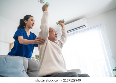 Asian older aged man doing physiotherapist with support from nurse. Senior elderly male sitting on sofa in living room using dumbbells workout exercise for patient with caregiver in nursing care. - Shutterstock ID 2157129949