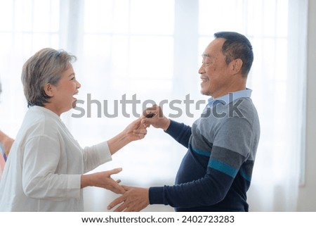 Asian Older male and females people dance with their partners on a dancing floor in living space. Happy older couple performing get exercise. Joyful carefree retired senior friends enjoying relaxation