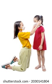 Asian Older Sister Putting The Face Mask To Her Younger Sister Isolated Over White Background