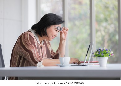 Asian Older Woman Wearing Eyeglasses Working With A Laptop Computer With Presbyopia Longsighted Eyes Problem And Fell Stessed.