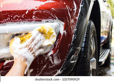 Asian Oldman Using Yellow Sponge Washing Front Fog Light Of New Red Car. Cleaning Background With Copy Space.