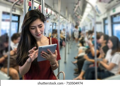 Asian oman passenger with casual suit using the technology tablet in the Skytrain rails or  subway for travel in the big city, lifestyle and transportation concept