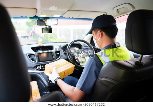 An Asian\
online delivery man holds a delivery box in his car and uses a\
scanner to verify the delivery. Online shopping service concept\
during coronavirus disease 2019\
(COVID-19)