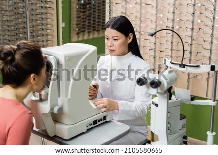 asian optometrist checking vision of blurred woman on ophthalmoscope in optics store