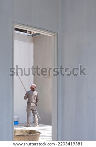 Asian Painter using Long handle Roller Brush to applying Primer white Paint on Concrete Wall in Door frame inside of House Construction Site