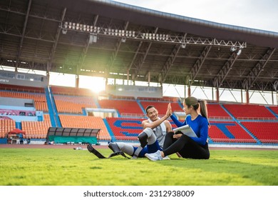 Asian para-athlete with prosthetic blades and trainer sit in stadium. Attractive amputee male runner and young sportswoman taking a break after practicing workout for Paralympics running competition - Powered by Shutterstock