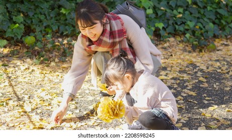 Asian parent and child picking up fallen leaves - Shutterstock ID 2208598245