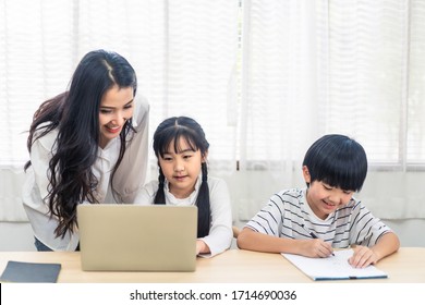 Asian Parent Teaching Homework To Children After Learning Online Education Class From School Teacher At Home. Mother Explaining Knowledge In Computer Laptop To Daughter And Helping Son Lecture Notes.