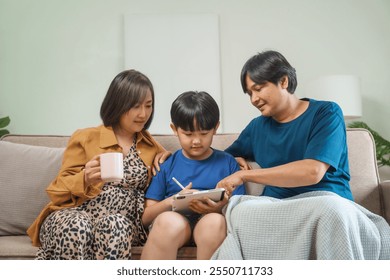 Asian parents and children sit together on a sofa at home, laughing and enjoying family time while using various devices like laptops, phones, and tablets, showcasing a tech-savvy lifestyle - Powered by Shutterstock