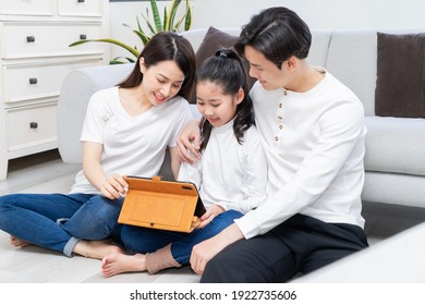 Asian parents are guiding their daughter to use the tablet
