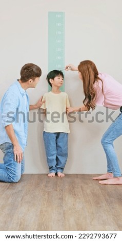 asian parents help their boy doing height measurement with his growing up and taller