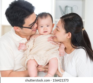 Asian Parents Kissing Six Months Old Baby Girl At Home.