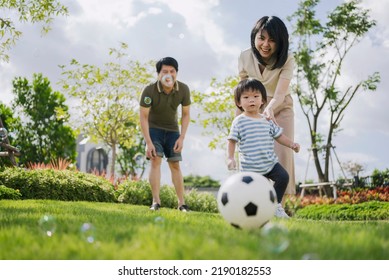 Asian Parents And Little Boy Playing Soccer In The Park Together. Happy Family Life Concept. 