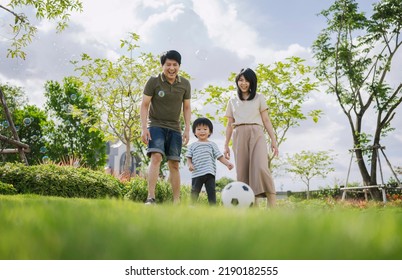 Asian Parents And Little Boy Playing Soccer In The Park Together. Happy Family Life Concept. 
