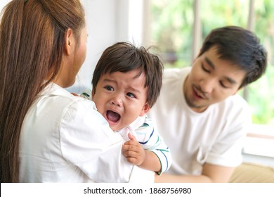 Asian Parents With Mother And Father Trying To Calm Down Crying Infant Son In Living Room At Home