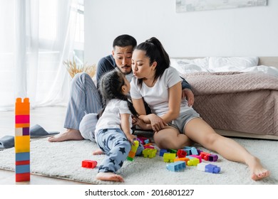 Asian Parents Pouting Lips Near Toddler Daughter And Building Blocks