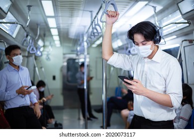 Asian Passenger Hand Holding On Handrail And Watching On Mobile Phone In Public Subway. People Wearing Mask To Prevent Virus Infection Or Dust.