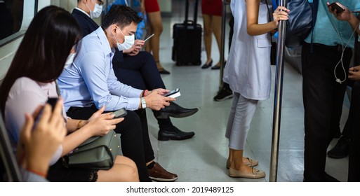 Asian Passengers Wearing Medical Face Mask Playing Smartphone Sitting On Public Subway Seat. New Normal Lifestyle And Social Distancing To Prevent Disease Infection