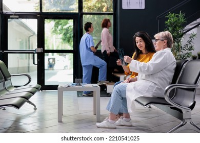 Asian Patient Analyzing Radiography Scan With Physician Specialist In Medical Clinic Lobby, Looking At Bones X Ray Exam Results To Find Disease Diagnosis. Doing Healthcare Consultation Appointment.