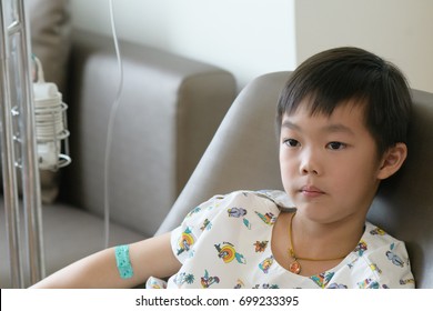 Asian patient boy with saline intravenous (iv) on hospital sofa, watching TV