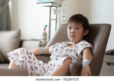 Asian patient boy with saline intravenous (iv) on hospital sofa, watching TV
