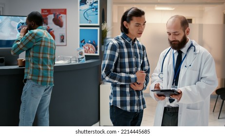 Asian Patient Chatting With Physician About Diagnosis On Digital Tablet, Explaining Disease To Give Support And Assistance In Hospital Reception. Examination Appointment And Checkup Visit.