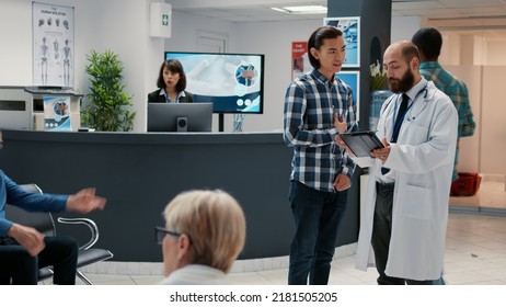 Asian Patient Discussing With Physician About Diagnosis And Treatment, Talking In Waiting Room Lobby At Hospital Reception Area. Healthcare Appointment For Checkup Visit Consultation.