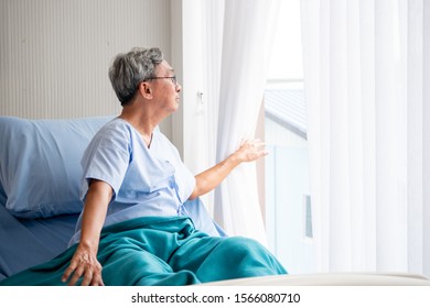 Asian Patient Man Looking Outside And Sitting On Hospital  Bed In The Hospital Room.