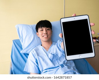 Asian Patient Sick Person Young Man Smile And Show Accident Or Health Insurance Claim Online In Tablet Mockup Screen Technology Device From Professional Agent Service While Lie Down On Bed In Hospital