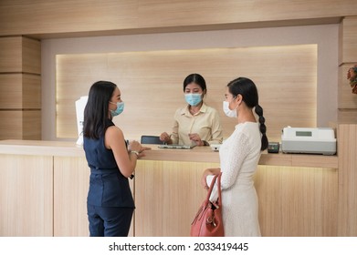 Asian patient woman wearing face mask with sister standing contact with receptionist at counter in the clinic
