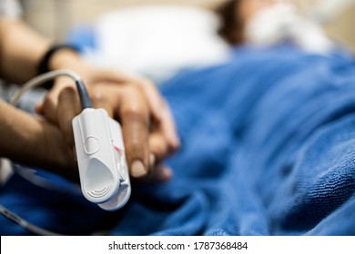 Asian patient's hand with an attached pulse oximeter on finger for monitoring,daughter holding her mother's hand,supporting comforting of seriously ill patient,intensive care in ICU room at hospital
