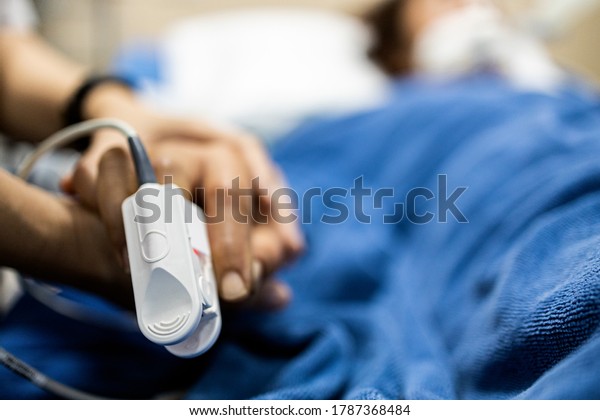 Asian patient\'s hand with an attached pulse\
oximeter on finger for monitoring,daughter holding her mother\'s\
hand,supporting comforting of seriously ill patient,intensive care\
in ICU room at hospital