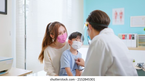 asian pediatrician with face shield and mask use stethoscope to exam sick boy when mother sit by in clinic - listen breath heartbeat through front chest