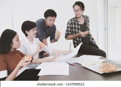 Asian People Eating Pizza Together During Lunch Break. In Office Meeting Room Discussing Work. Muted Tone.