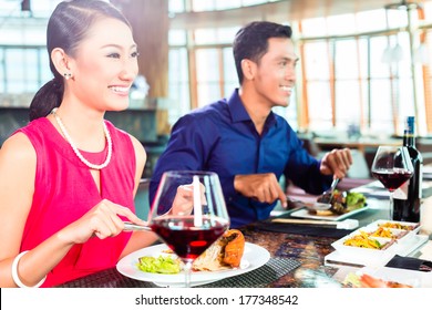 Asian People Having Dinner And Drinking Red Wine In Very Fancy Restaurant With Open Kitchen In Background