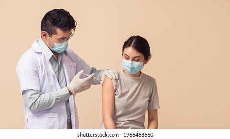 Asian People, Man Doctor Wearing Medical Mask And Gloves Giving Coronavirus (COVID-19) Vaccine To Female On Brown Background. Asian Woman Getting Vaccinated By Medical Professional.