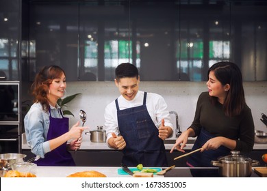 Asian People. Man And Woman Cooking Dinner For Guests. Young People Are Enjoying Cooking. Group Of Friends At Home Party.