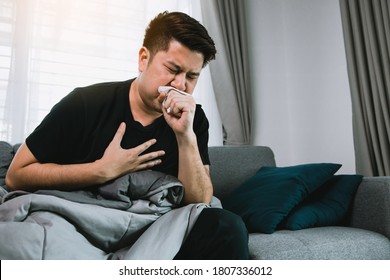 Asian People Are Sick Or Ill With Bronchitis While Coughing By Covering Their Mouth With Tissue Paper When He Sit On The Sofa At Home.