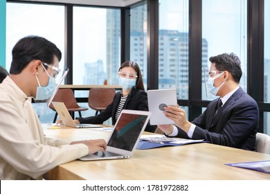 Asian People Working Together In Co-working Space Following Social Distancing And New Normal Policy By Wearing Facial Mask In The Business Office Workplace During Covid-19 Outbreak(focus On Right Man)