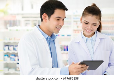 Asian Pharmacist Team Looking At Tablet Computer In Chemist Shop Or Pharmacy