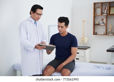 Asian Physiotherapist Showing Results Of Medical Tests To Young Patient