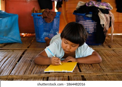 Asian poor child doing homework at a small house. The poor student is writing something on the book.