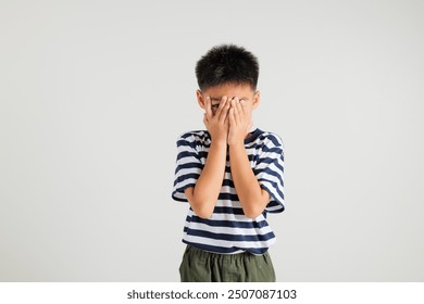 Asian portrait young kid boy in depressed bad mood covering face with hands and peering out with one eye between fingers studio shot isolated on white background, primary child surprised and shocked - Powered by Shutterstock