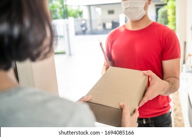 Asian Postman Or Deliveryman Carry Small Box Deliver To Young Woman Customer In Front Of Door At Home. Man Wearing Mask Prevent Covid Or Coranavirus Affection Outbreak. Social Distancing Work Concept.