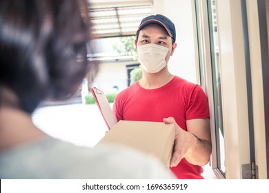 Asian Postman Or Deliveryman Carry Small Box Deliver To Young Woman Customer In Front Of Door At Home. Man Wearing Mask Prevent Covid Or Coranavirus Affection Outbreak. Social Distancing Work Concept.