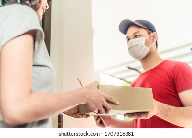 Asian Postman Or Deliveryman Carry Small Box Deliver To Young Woman Customer In Front Of Door At Home. Man Wearing Mask Prevent Covid Or Coranavirus Affection Outbreak. Social Distancing Work Concept.