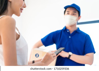 Asian Postman Or Deliveryman Carry Small Box Deliver To Young Woman Customer In Front Of Door At Home. Man Wearing Mask Prevent Covid Or Coranavirus Affection Outbreak. Social Distancing Work Concept.