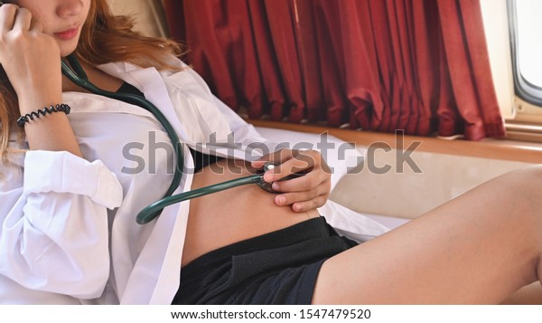 Asian pregnancy female use\
stethoscope listening heart rate of fetus in Recreational\
vehicle.
