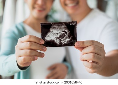 Asian pregnant couple feeling happy show ultrasound image at home, focus on ultrasound image - Powered by Shutterstock